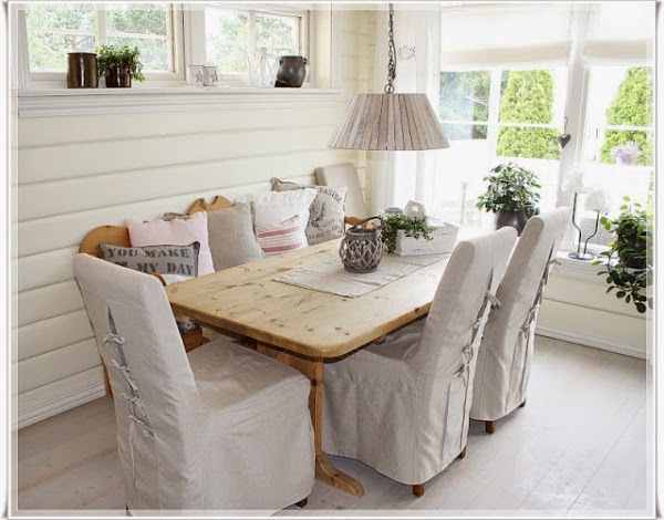 Wiejski stół z naturalnego drewna,krzesla w dekoracyjnych białych ubrankach i biała lampa na łańcuchu w aranżacji jadalni