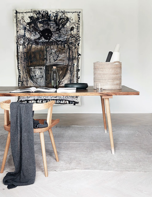 Surowy drewniany stół i krzesło,betonowa posadzka , batikowe obrazy w czerni i beżach