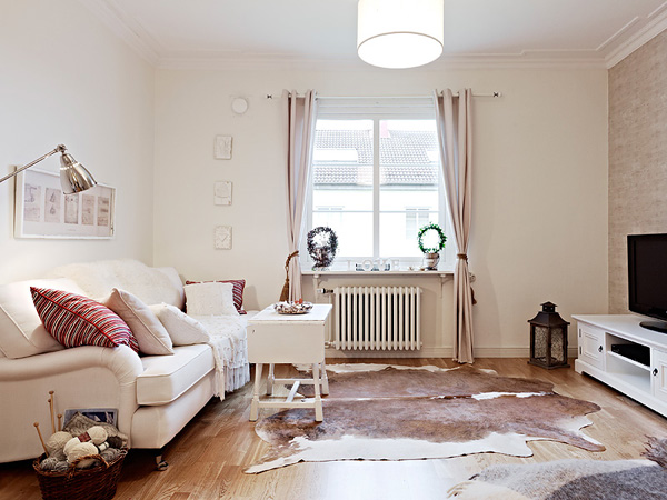 Biała sofa,zasłony,drewniany stolik kawowy i bydlęca skóra na podłodze w salonie