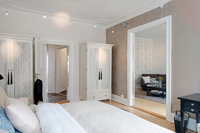 Białe szafy ze szprosami w skandynawskiej sypialni