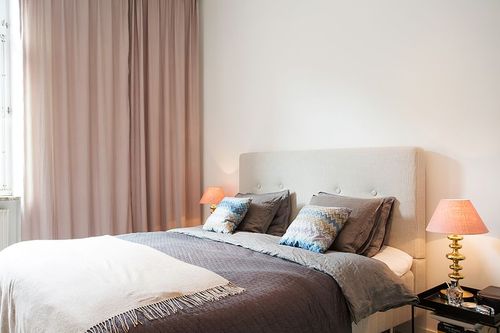 Biało-beżowa sypialnia skandynawska z poduszkami na łóżku z wzorem kolorowego szewronu