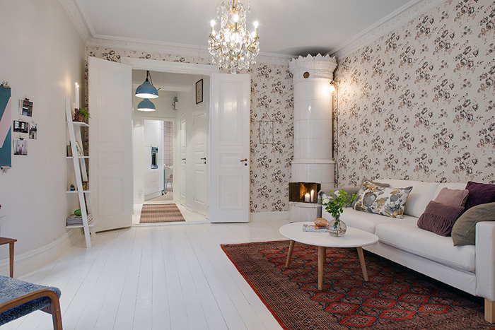 Skandynawski salon z kwiecistą tapetą,etnicznym dywanem,biała drabinką i okragłym piecem