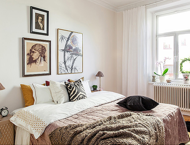 Grafiki i fotografie retro w aranżacji białej sypialni z beżową narzutą na łóżku