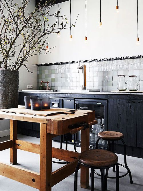 Drewniany stół roboczy w stylu industrialnym w czarnej kuchni z wiszącymi żarówkami na kablach