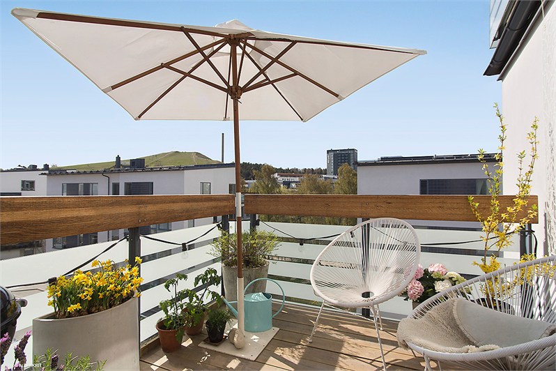 Białe ażurowe fotele, parasol i drewniany podest  w aranżacji małego balkonu