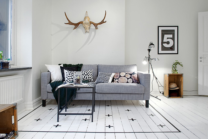 Skandynawski biały salon z szarą sofą i podłogą z pomalowanych desek
