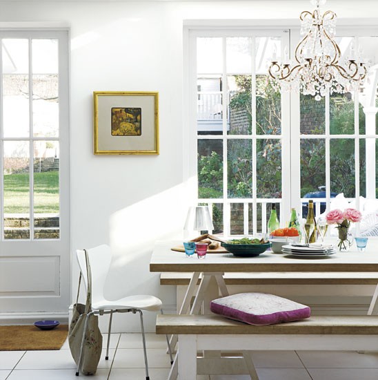 Aranżącja białej jadalni z drewnianym stołem,nowoczesnymi krzesłami i kryształowym żyrandolem