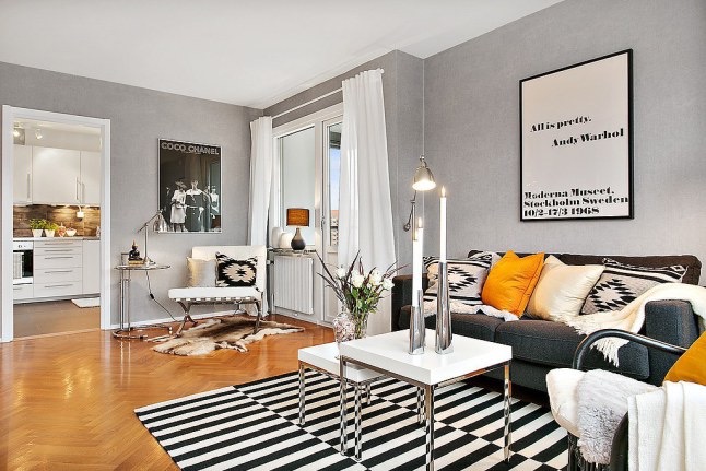 Nowoczesny biało-szary salon skandynawski z zółtymi i biało-czarnymi etnicznymi poduszkami na grafitowej sofie