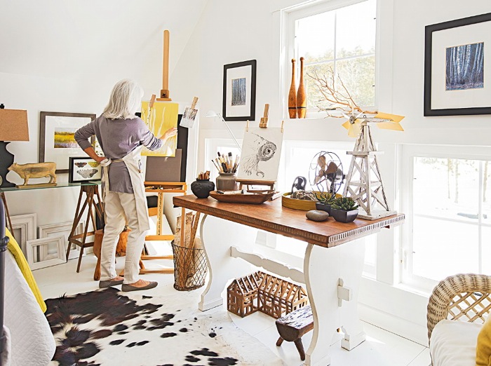 Domowa pracownia w wiejskim stylu z rustykalnym stolem na profilowanej białej podstawie,wikinowe i drewniane pojemniki,dywan biało-czarny z bydlęcej skóry,dekoracyjne gałązki i biały lampion na stole
