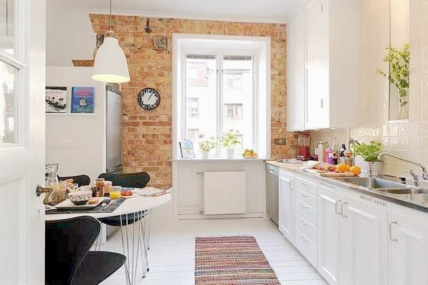 Aranżacja białej kuchni skandynawskiej ze ścianą z czerwo9nej cegły i białą pidłogą