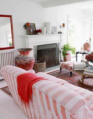 Sofa w biało-czerwone paski,czerwone lustro i czerwone amfory i dekoracje w białym pokoju kominkowym