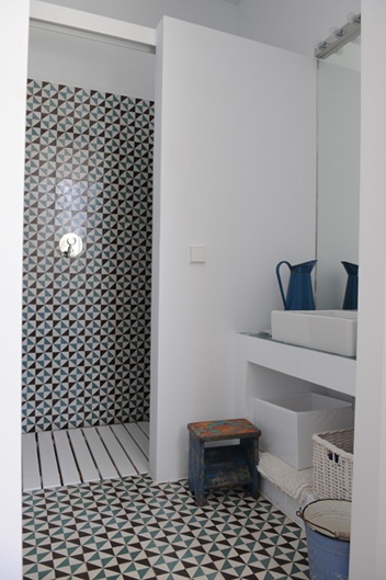 Murowane białe półki w łazience,drewniany ażurowy podest w kabinie,wzorzysta glazura w hiszpańskim stylu,stołek vintage,niebieskie metalowy dzban na wodę w śródziemnomorskiej łazience
