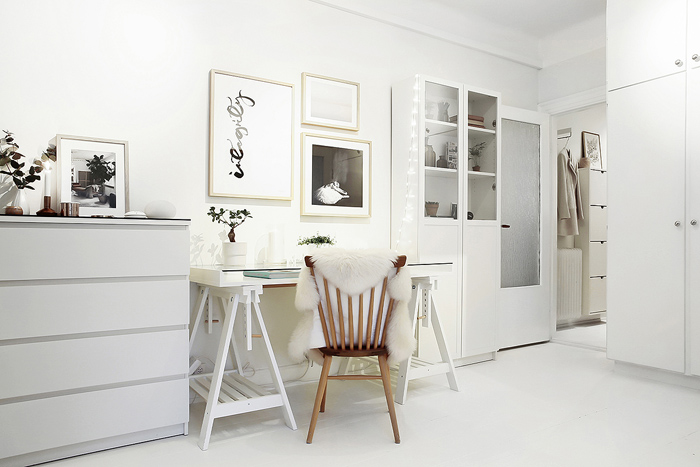 Kącik z białym biurkiem na kozłach w stylu skandynawskim,biała komoda i witryna,czarno-białe grafiki na ścianie