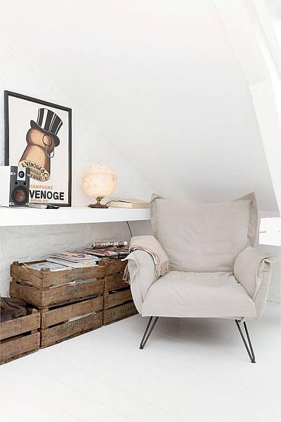 Nowoczesny fotel z poduchami z bawełny, drewniane skrzynki,murowanan wapienna półka i nowoczesny plakat na białej ścianie