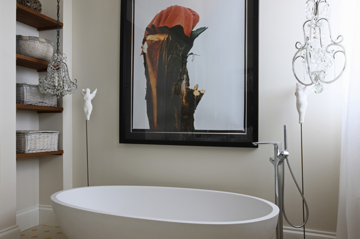 Drewniane półkiz wiklinowymi pojemnikami we wnęce ściany w łazience z owalną wanną, żyrandolem i nowoczesnym obrazem na ścianie