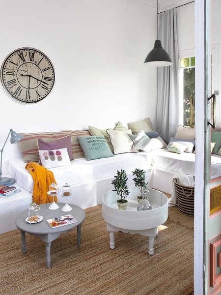 Stylowe okragłe stoliki vintage,rustrykalny duzy zegar na ścianie,kolorowe poduszki na białej sofie