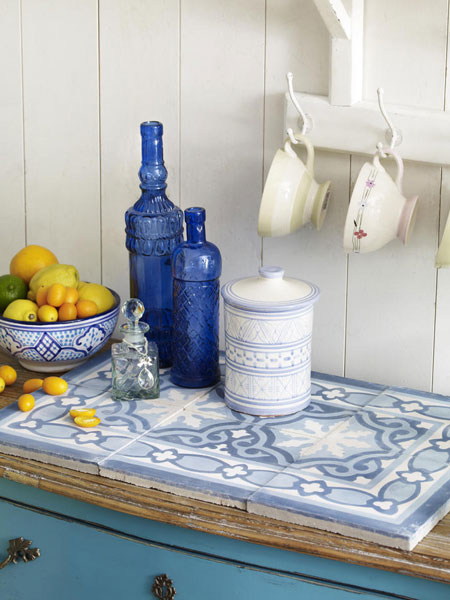 Śródziemnomorskie płytki w aranżacji kuchni z niebieska komodą i butelkami w kolorze indygo