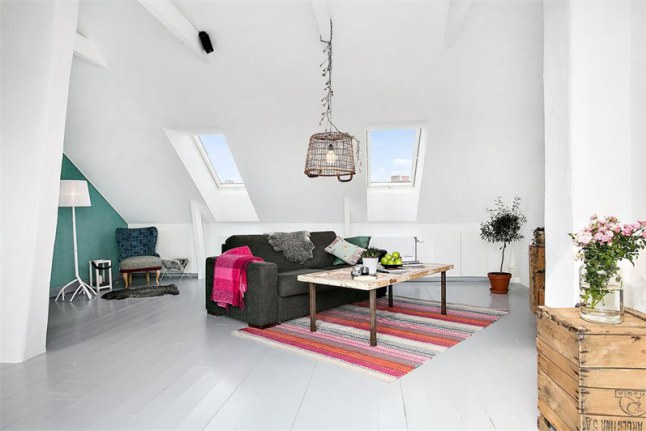 Białe deski na podłodze,skandynawski dywanik w paski,szara sofa,drewniane skrzynki i druciana lampa w salonie