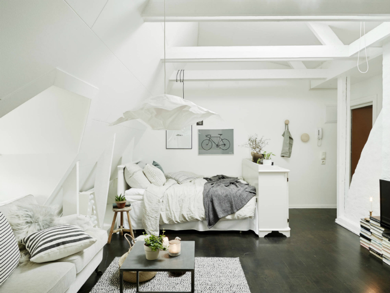 Salon razem z sypialnią w białej aranżacji małego mieszkania na poddaszu