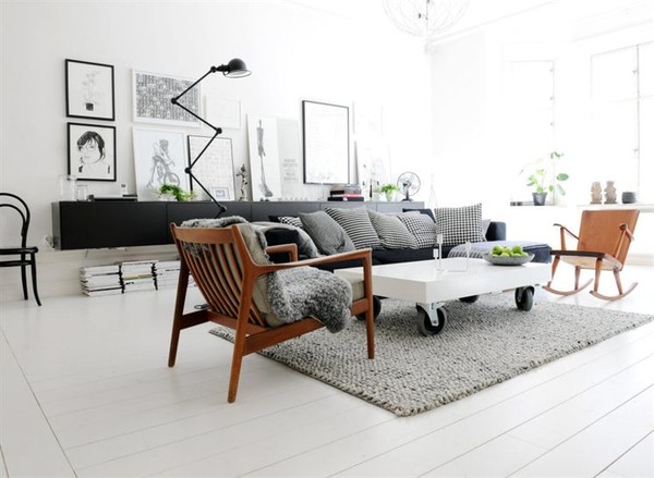 Biały stolik na kólkach,drewniane fotele z lat 60-tych,szara sofa nowoczesna i czarna komoda z lampą na przegubach w salonie z galerią skandynawskich grafik