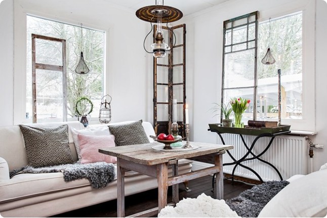 Rustykalna lampa nad bielonym stolikiem kawowym,biała sofa i okna w stylu vintage w roli dekoracji skandynawskiego salonu