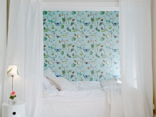Turkusowo-błękitna tapeta we wzory w białej sypialni