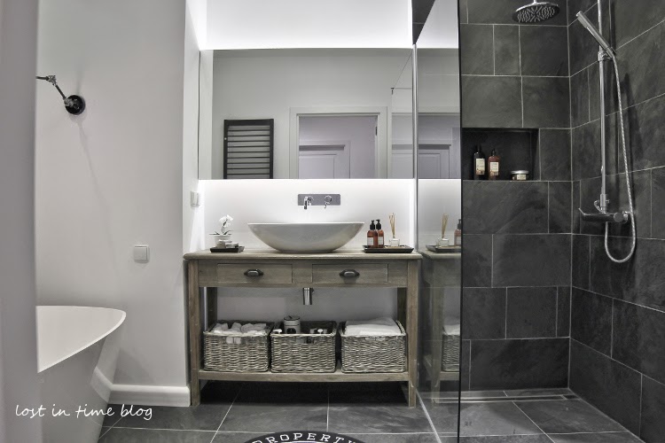 Piękna łazienka z owalną wanną,z bieloną skandynawską konsolką z półką i uywalką,grafitowe matowe płytki na ścianie i w kabinie z natryskiem