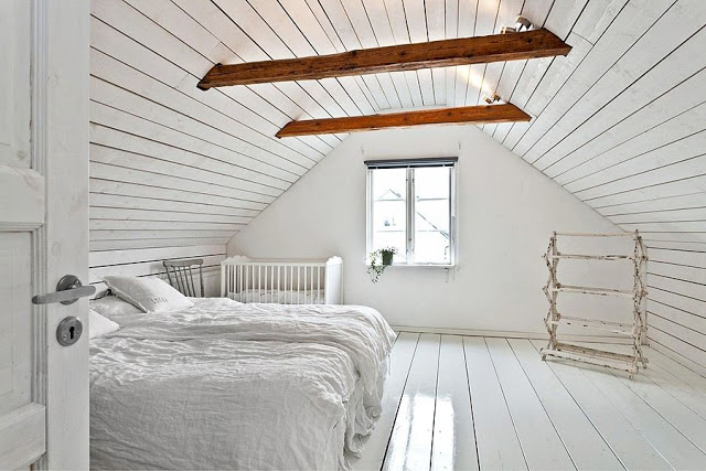Biala sypialnia na poddaszu z drewnianymi belkami