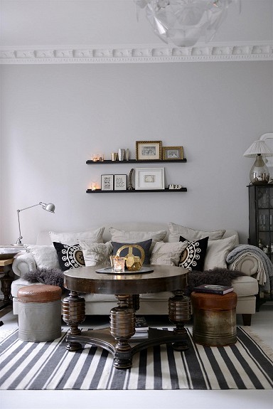 Stylowy okrągły stół,metalowe industrialne pufy i dywan w czarno-białe paski w szarym salonie