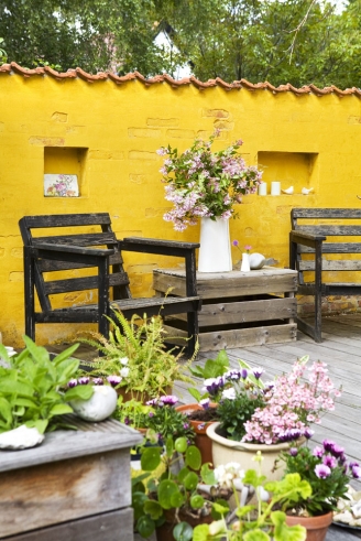 Żółta ściana na wiejskim tarasie z prostymi drewnianymi fotelami i skrzynką