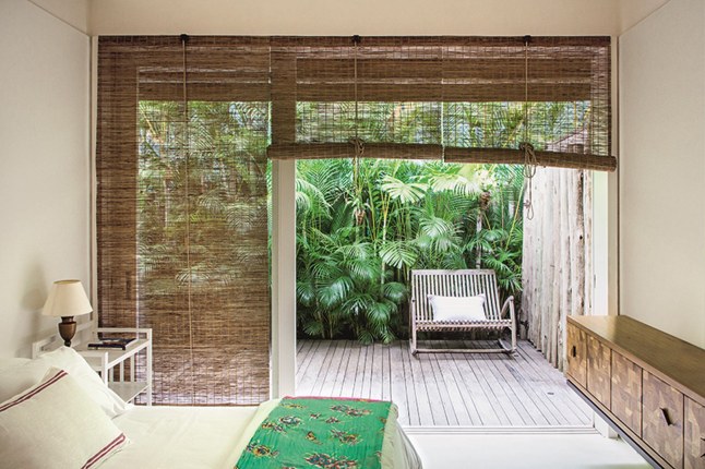 Bambusowe zwijane rolety w oknach,drewniane komody i nowoczesne fotele w aranżacji sypialni
