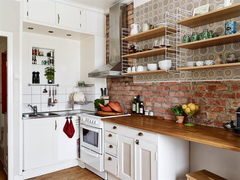 Mała biała kuchnia z drewnianym blatem i ścianą z czerwonej cegły