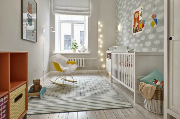 Szara tapeta w chmurki na ścianie w pokoju dla dziecka,fotel na płozach i girlanda z bawełnianymi kulami z żarówkami