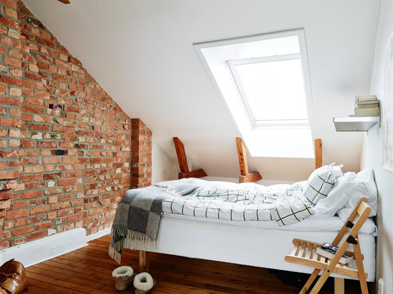 Biała sypialnia pod skośną ścianą i ścianą z czerwonej cegły