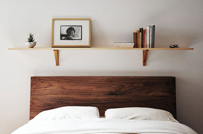 Drewniana pojedyncza półka nad brązowym łóżkiem