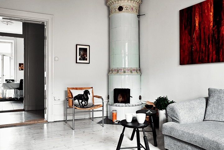 Skandynawski bialy salon z ceramicznym piecem, szarą sofą,i nowoczesnym obraze, w brązach