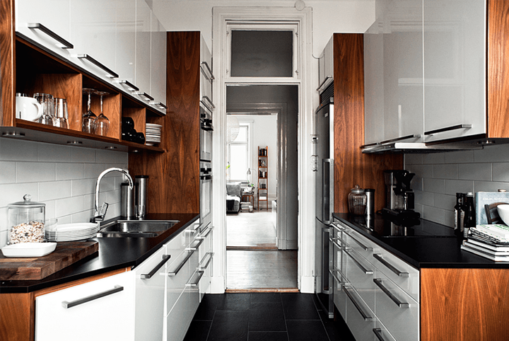 Drewniane boki szafek i czarne blaty w malej białej kuchni