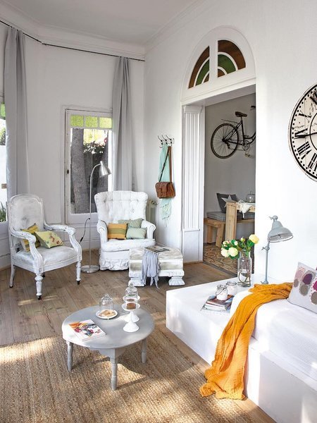 Szare zasłony,białe stylowe fotele,drzwi ze świetlikami,okrągły szary stolik kawowy i duży rustykalny zegar na białej ścianie