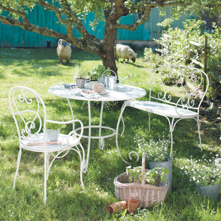 Białe kute meble ogrodowe w deserowej aranżacji w letnim ogrodzie