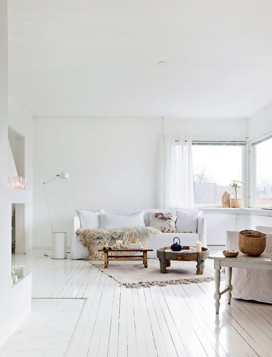 Białe malowane deski na podłodze w salonie,białe sofy,drewniane stoliki i ławy w stylu skandynawskim,futrzaki,lampa podłogowa biała z wysięgnikiem
