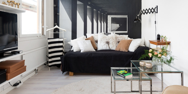 Czarna sofa z białymi i jasno-brązowymi poduszkami na tle ściany z fototapetą,metalowe kwadratowe stoliki ze szkłem i jasna podłoga z drewna w salonie