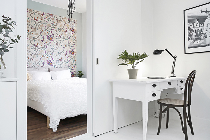 Skandynawskie białe biurko z szufladami,czarne gięte krzesło z drewna,biała podłoga i kwiatowa tapeta na ścianie przy łóżku