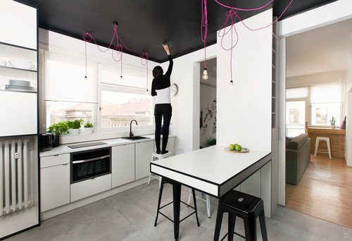 Białe meble , różowe kable z żarówkami i czarny sufit i ściany nad szafkami kuchennymi