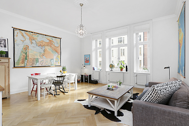 Mapa fizyczna świata na ścianie w salonie z białym stołem,różnymi krzesłami, szarą sofą i drewnianym białym stoliek kawowym w stylu shabby