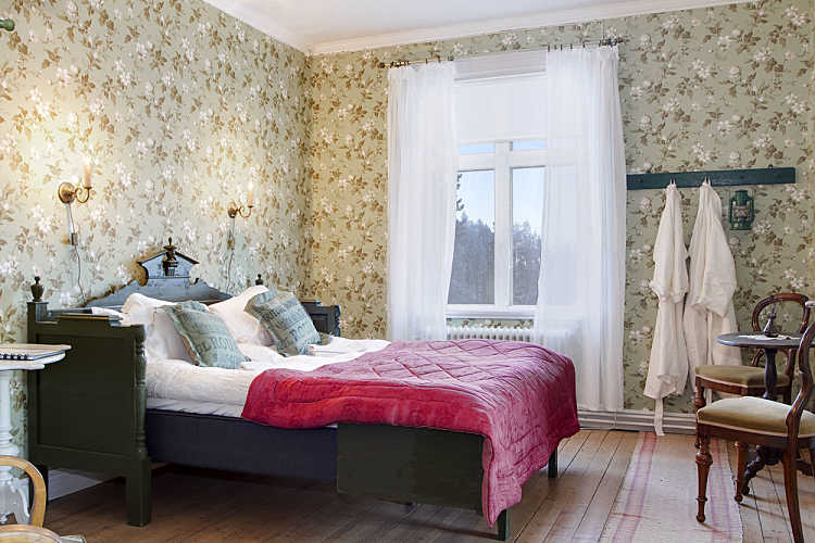 Tapeta w kwiaty,stylowe drewniane łóżko i białe firanki w eklektycznej sypialni