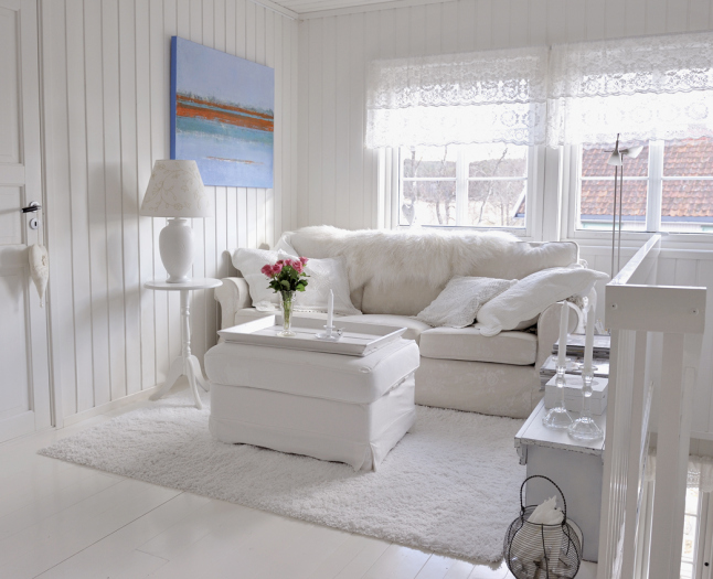 Biała sofa,podnóżek,biały dywan i biały okragły stolik z lampą w białym saloniku