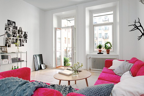 Różowa sofa i szare wełniane pledy w białym salonie w stylu skandynawskim