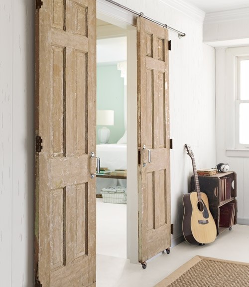 Drewniane drzwi wrota przesuwane na białej ścianie w salonie, sizalowy dywan i szafka niska z drewna
