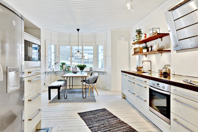 Skandynawska biała kuchnia z czarnymi blatami,bielonymi deskami na podłodze i metalowym stołem z drewnianym blatem
