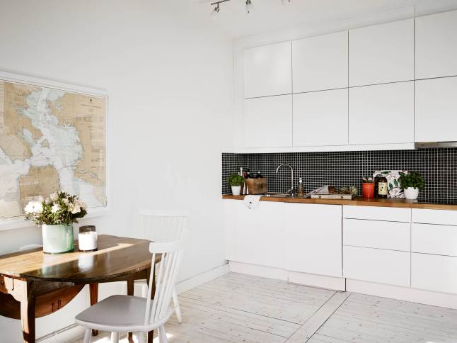 Biała minimalistyczna kuchnia z czarną glazurą na ścianie,drewniany składany stół i białe skandynawskie krzesła z drewna w kuchni